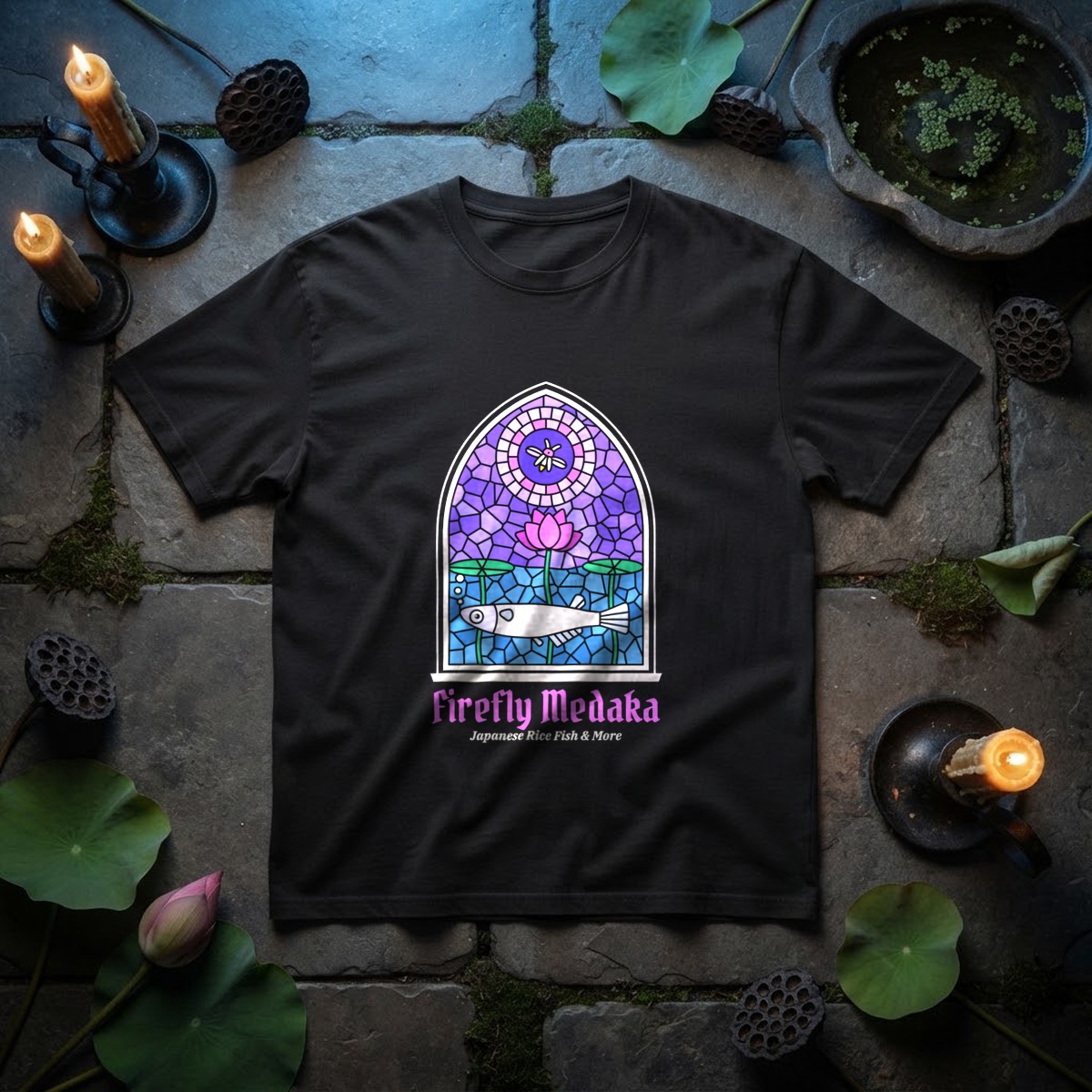 Cathedral Pond stained glass medaka t-shirt in black on old stone flagstones with lotus leaves, a lotus bud, dried lotus pods, a stone dish of duckweed, and iron candlesticks