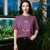 Woman with long dark waves wearing the Nocturne logo tee in Berry, in a Victorian greenhouse with a large planted aquarium