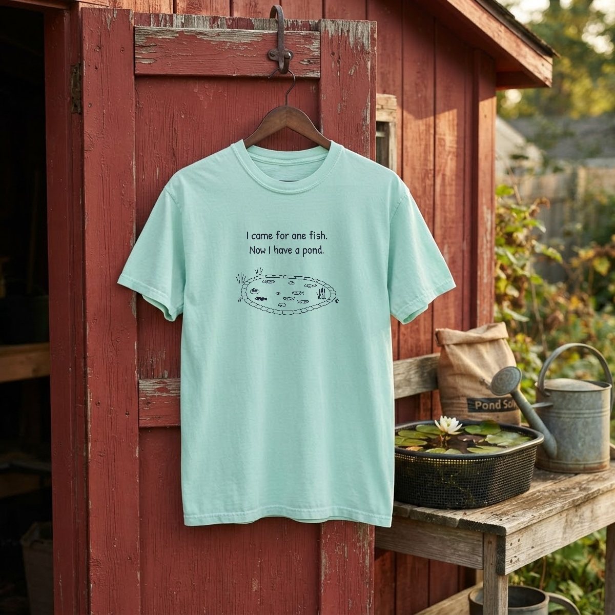 I came for one fish, now I have a pond t-shirt in chalky mint on a hanger on a red garden shed door, beside a potting bench with a water lily in a planting basket