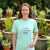 Woman with long auburn hair wearing the Rice Fish, Not a Sushi Order tee in Chalky Mint, on a sunny deck with glazed container ponds